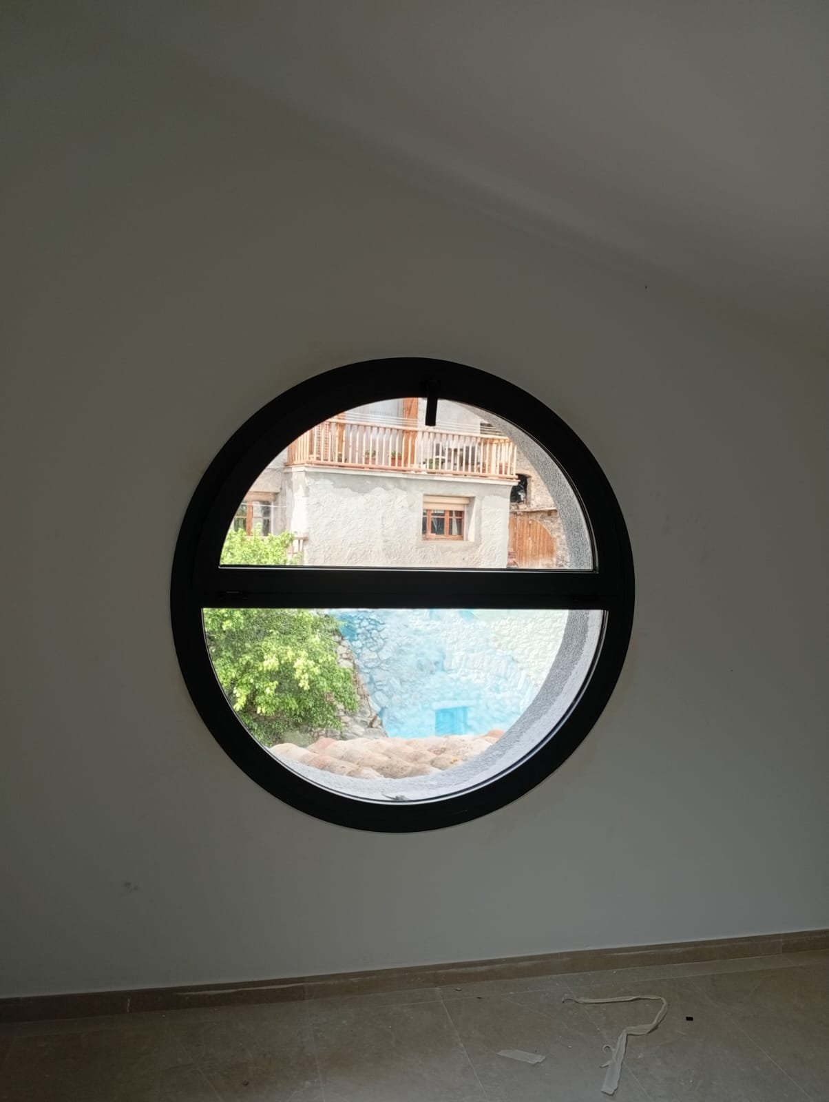 Ventana circular de aluminio negro con vistas al pueblo