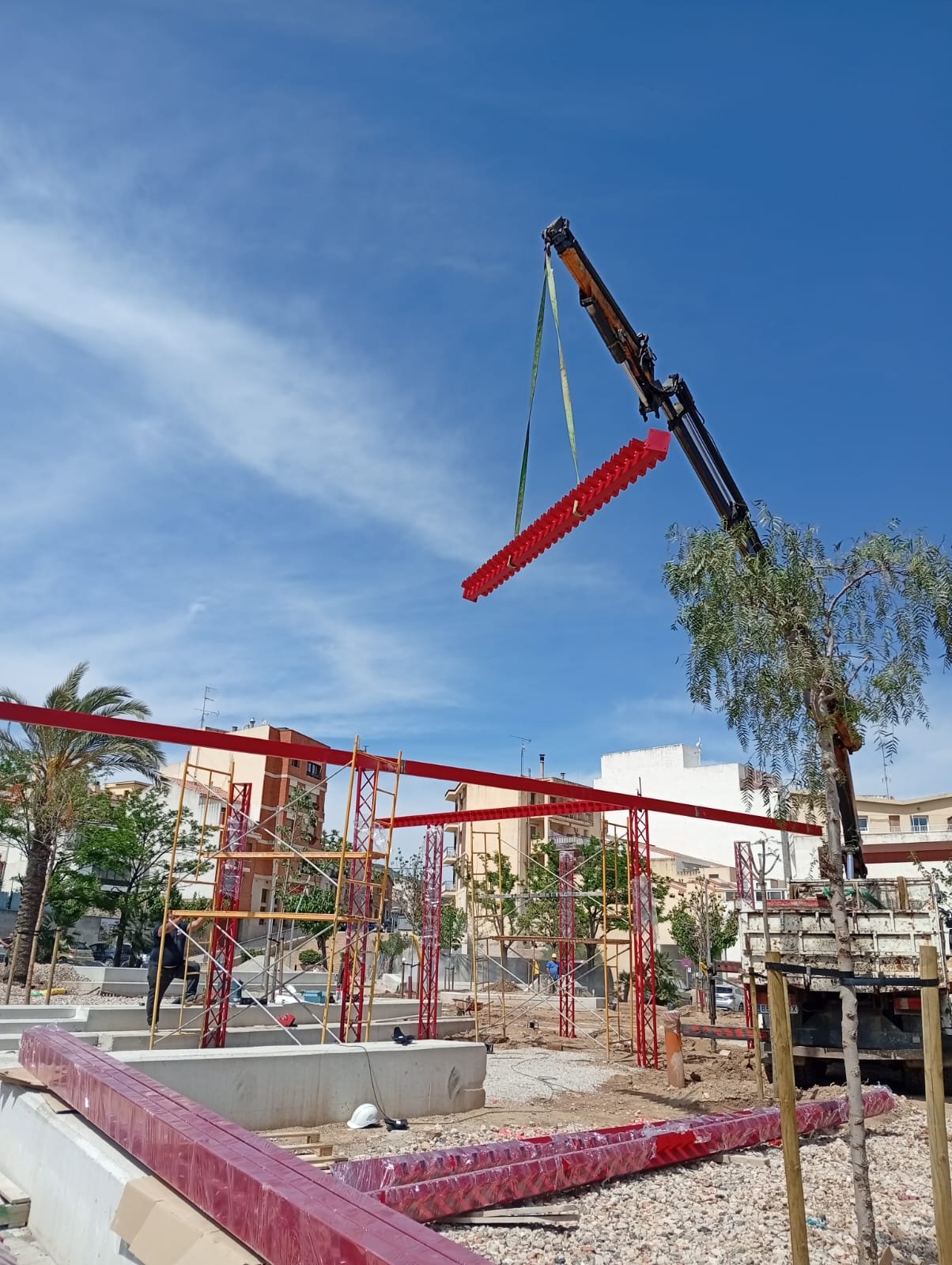 Viga de acero roja izada con grúa durante el montaje de una estructura en obra