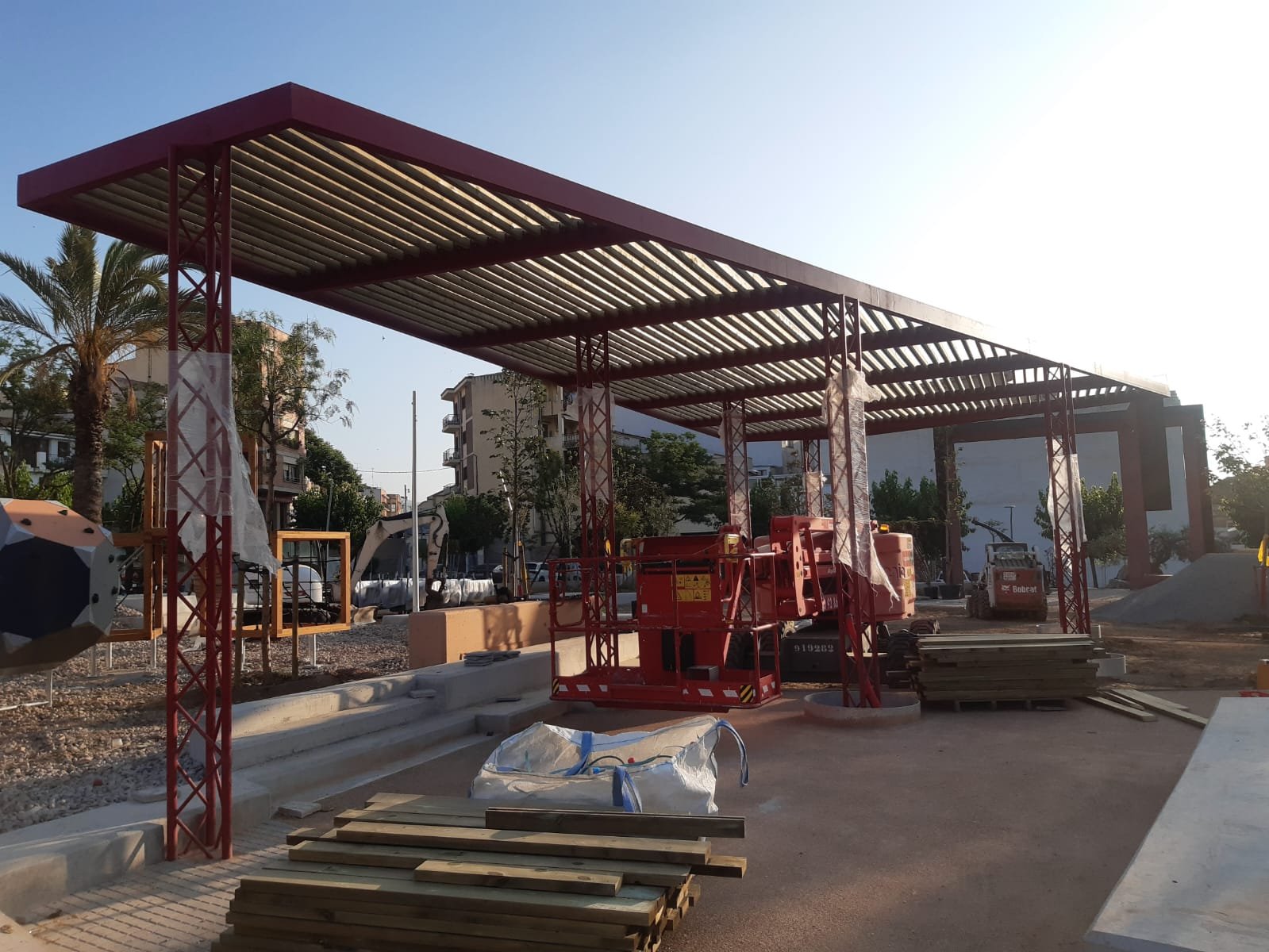 Pérgola terminada de acero rojo con celosía de madera en una plaza